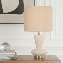 Load image into Gallery viewer, Beige table lamp on a wooden surface with books and a decorative object in the background.
